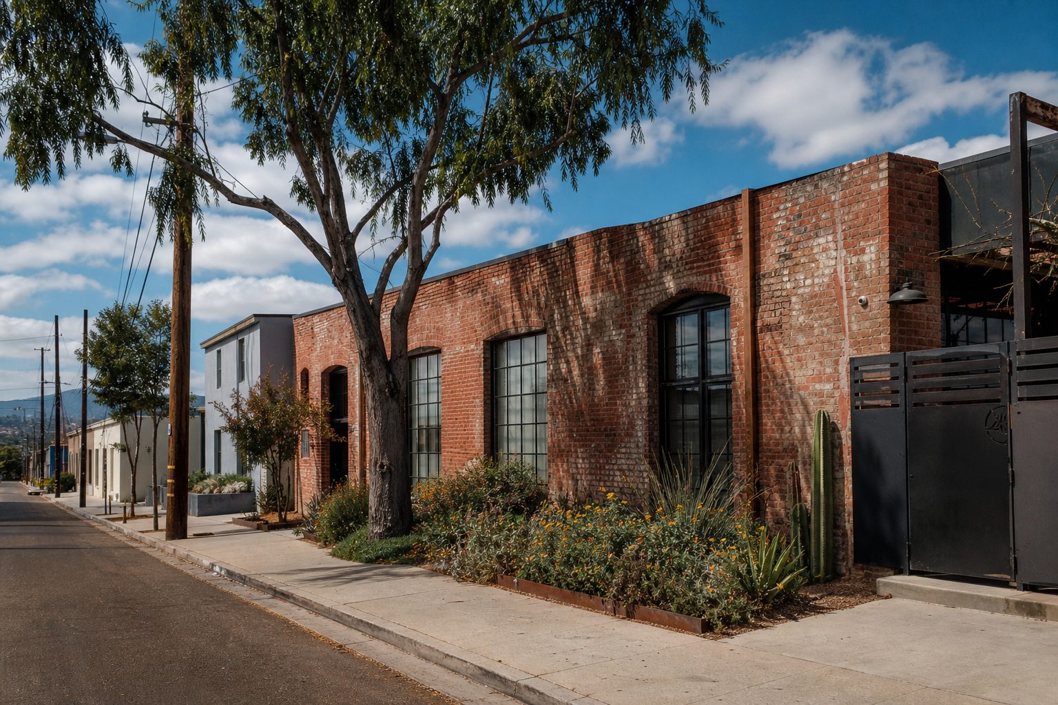 Corner brick warehouse conversion with industrial windows and native plantings in Barrio Logan's walkable arts district on a sunny October morning.