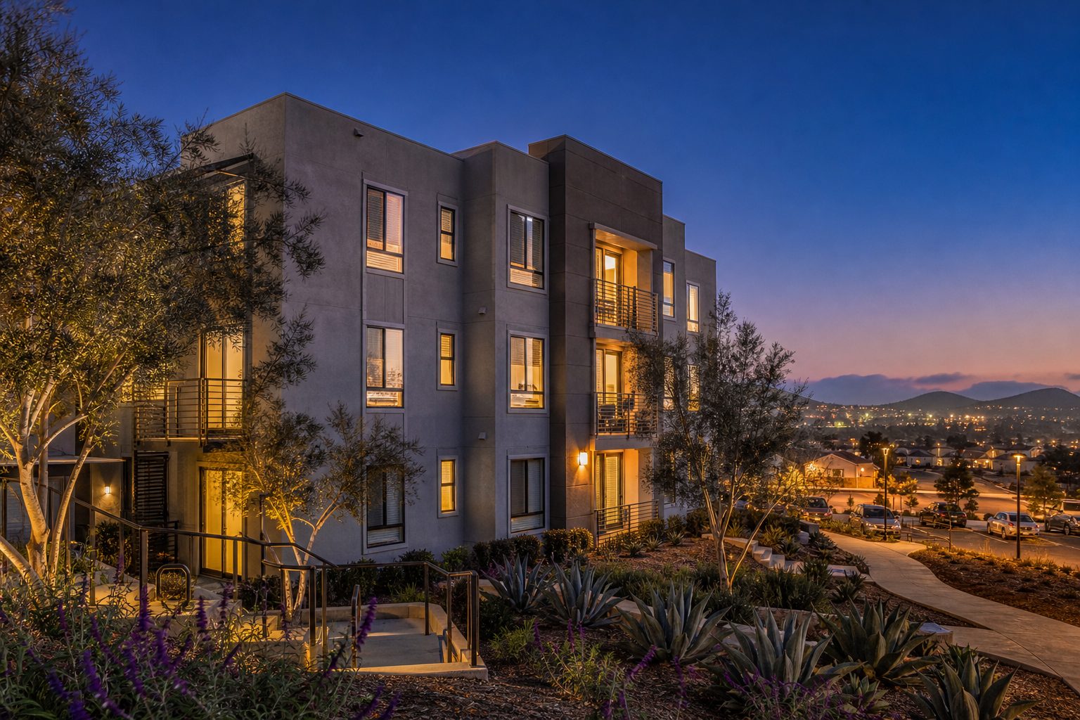Three-story multi-family residential building at dusk with native landscaping and interior lights in Vista, East County San Diego