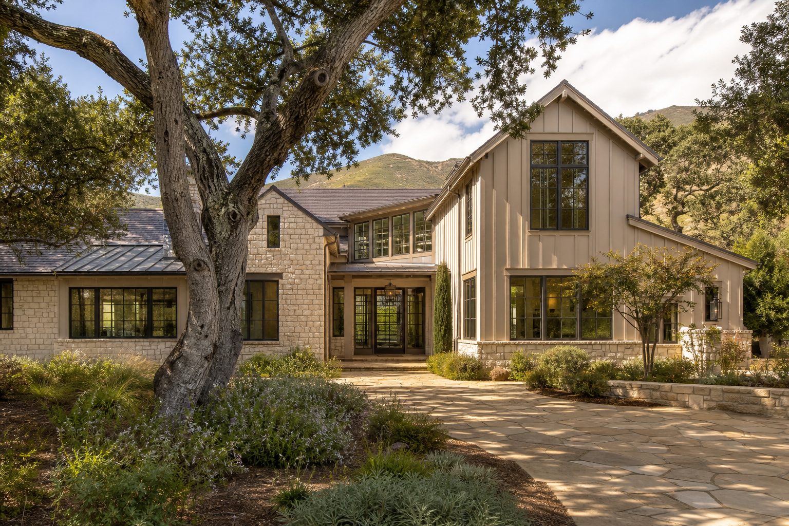 Luxury transitional home in Carmel Valley with stone exterior, mature oaks, and professional landscaping in afternoon light.