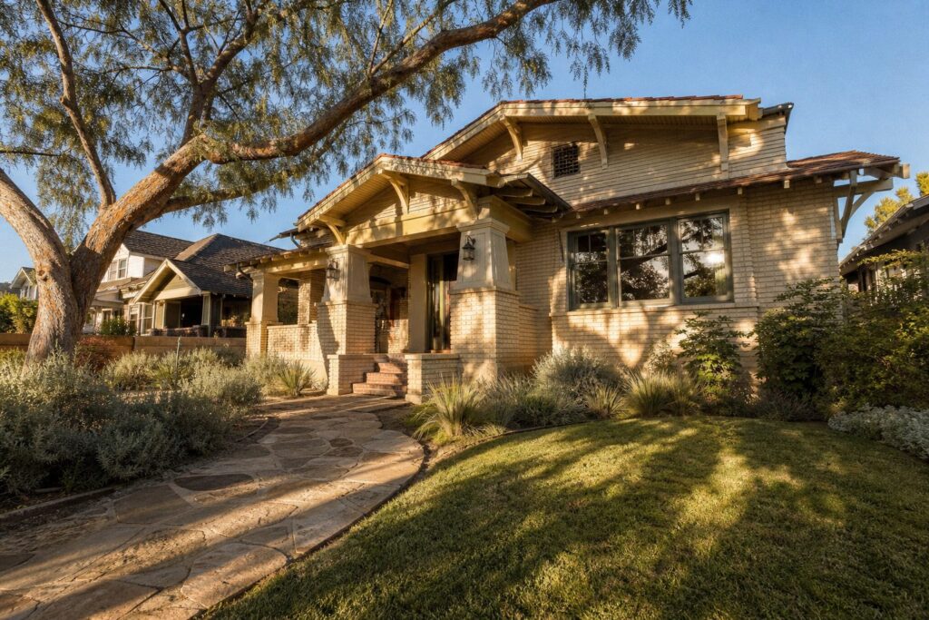Cream-colored Craftsman bungalow with deep eaves and front porch in North Park historic district, dappled shade from mature pepper tree.