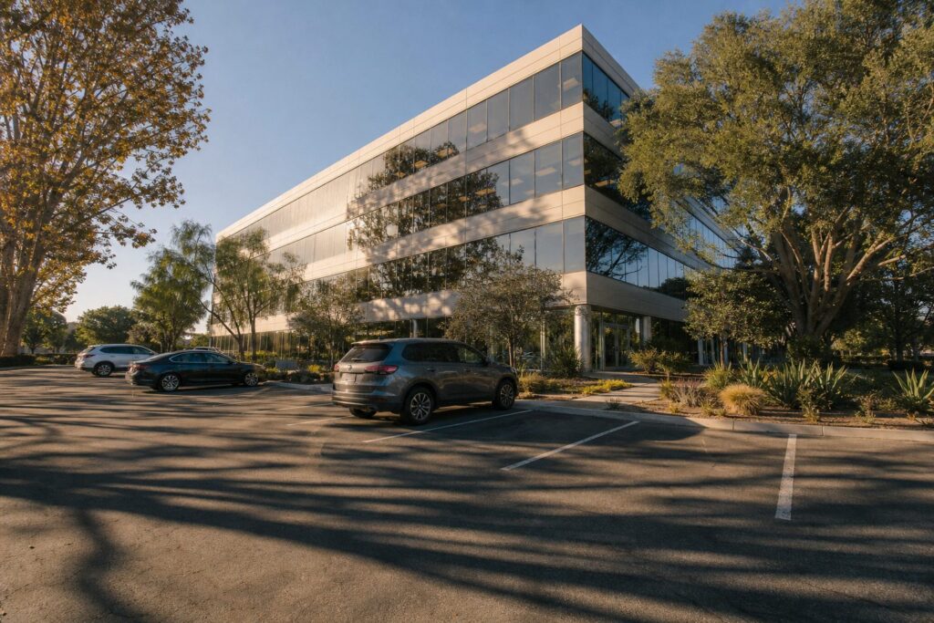 Modern three-story office building with glass lobby in Kearny Mesa industrial park at sunset with parked vehicles and native landscaping.