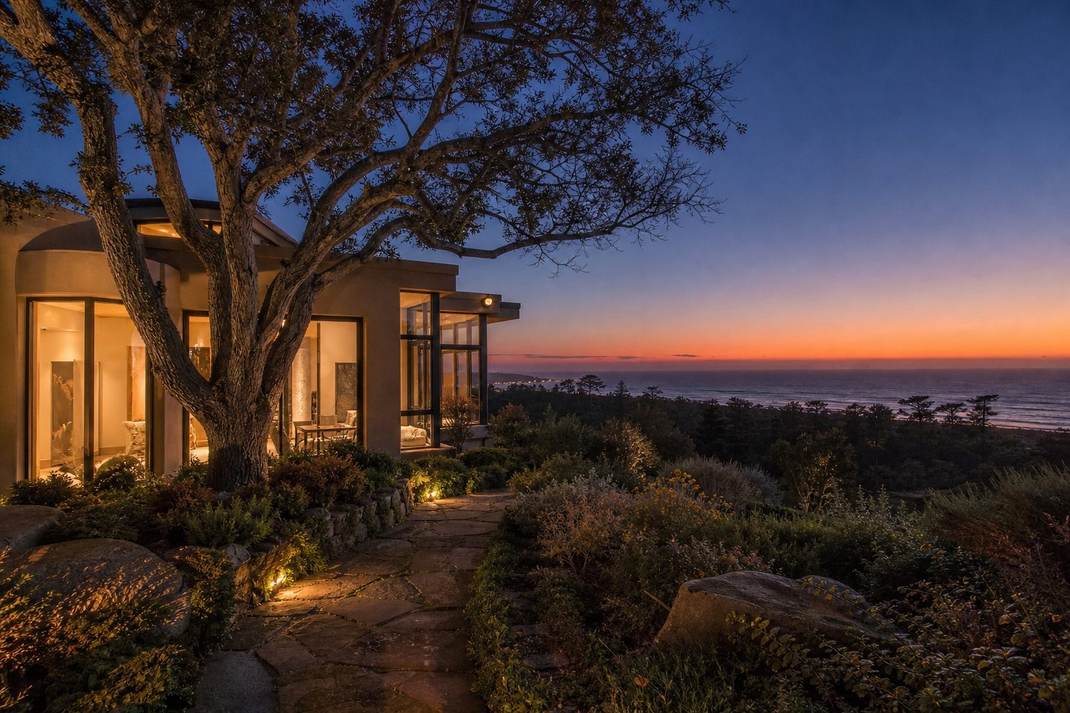 Luxury Muirlands home at twilight with interior glow, mature oak tree, and ocean sunset view in background.