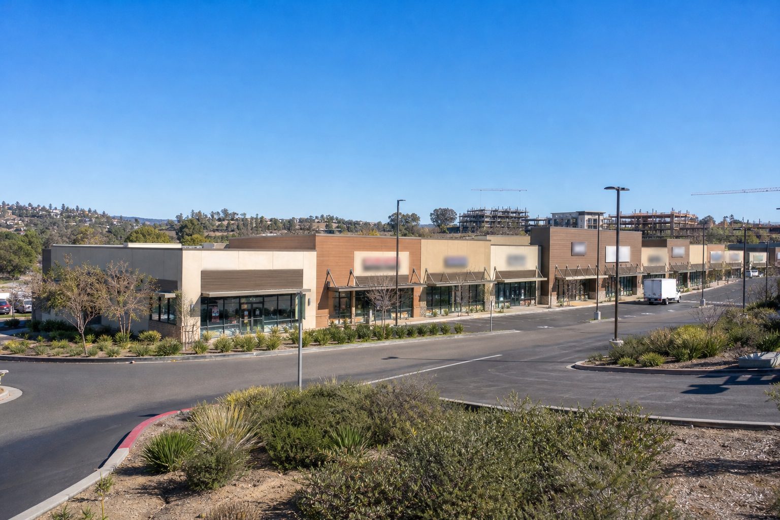 Multi-tenant retail strip center in Mission Valley with stucco exterior, landscaped frontage, and construction activity visible in distance.